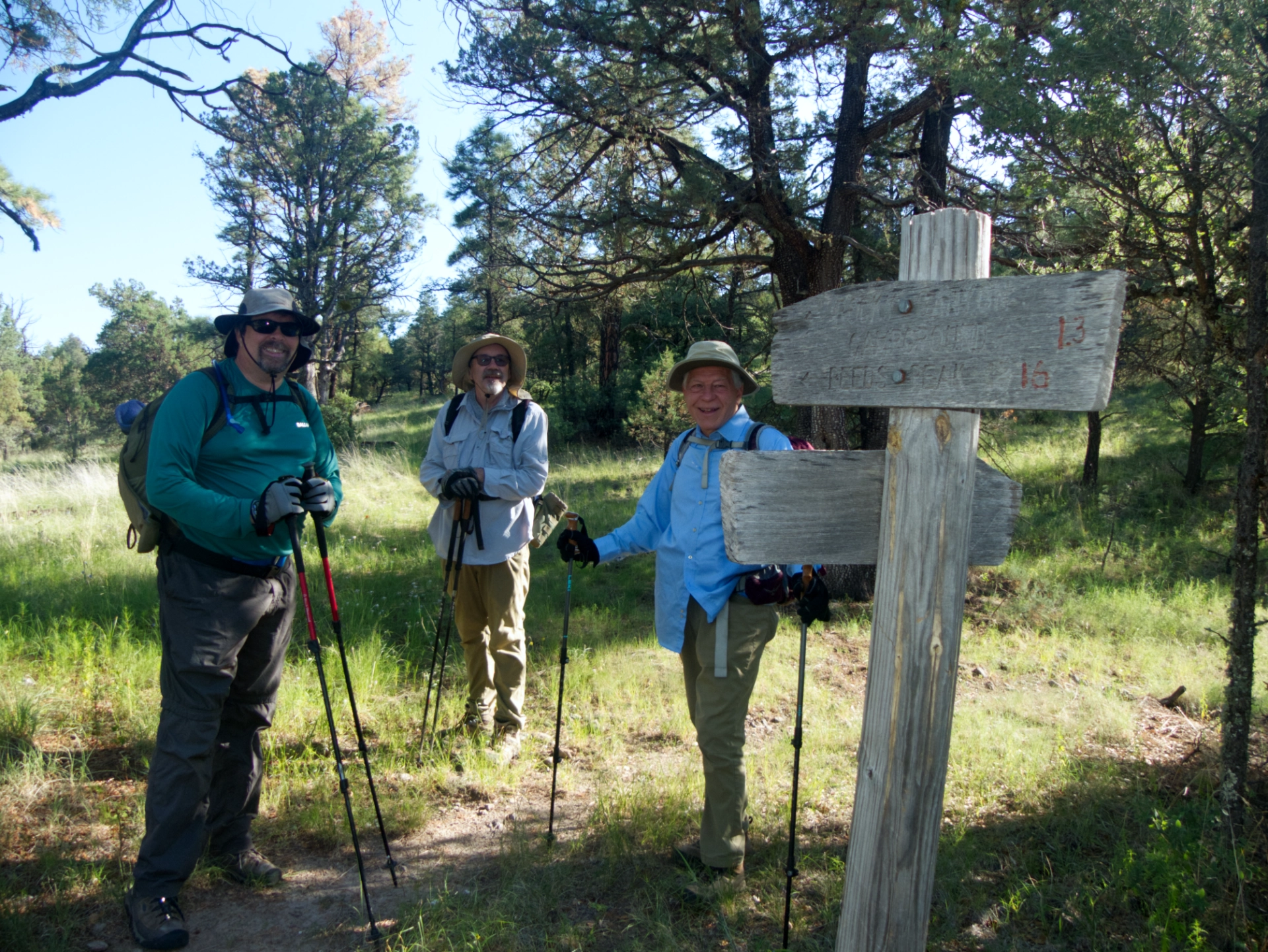 Three hikers posing by an old trail sign