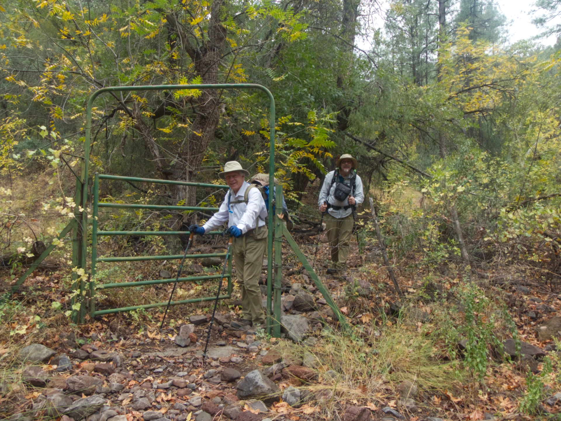 smiling hikers at a metal gate by a creek