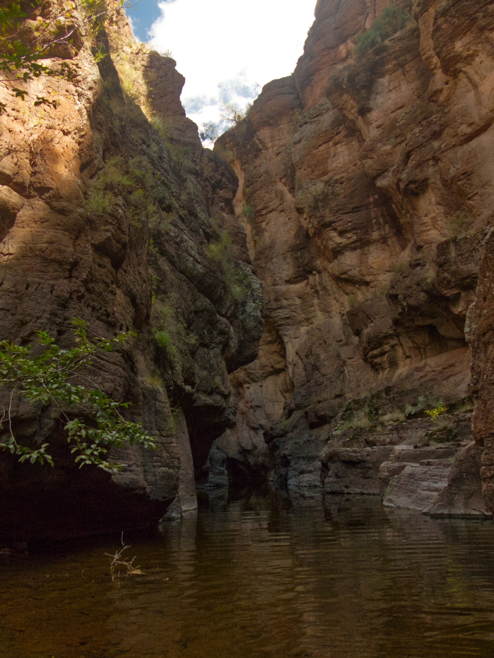 very narrow and dark slot canyon with a deep pool at the base