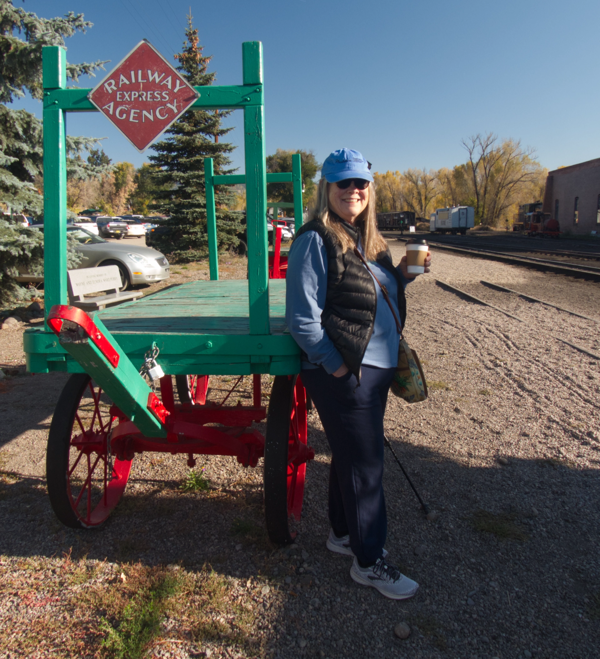 Ann enjoying her coffee next to an old wooden baggage trolley